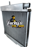 A silver aluminum radiator with a top inlet pipe, shown on a plain white background with a large 'Lucky's Fab Shop' logo overlay on the front.
